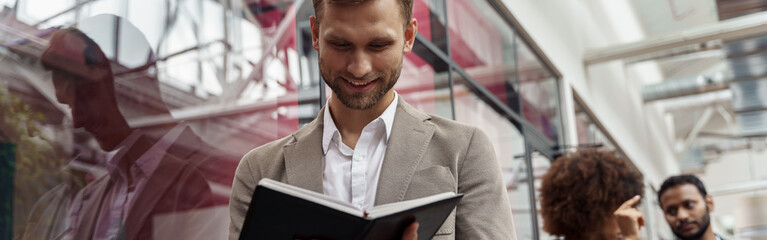 Wall Mural - Businessman looks into notepad while standing in office against background of colleagues