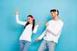 Portrait of two satisfied positive funny persons dressed white shirts dancing having fun enjoy music isolated on blue color background