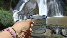 Inspirational Quote - You Can't Pour From An Empty Cup. Take Care Of Yourself First. With Person Holding Traditional Empty Cup Against The Waterfall Background. Self Care And Love Concept.