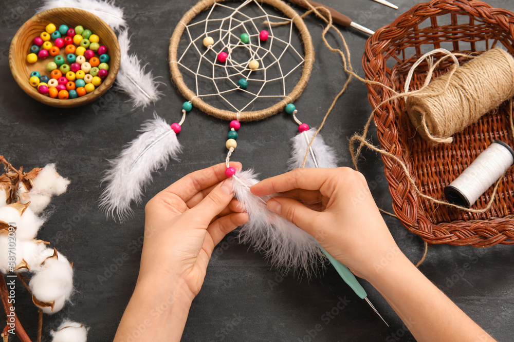 Woman making dream catcher on dark table, closeup