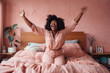 © Trinette Reed - Ecstatic joyful Black curvy woman dressed in pink in bedroom laughing.