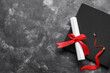 © Pixel-Shot - Diploma with red ribbon and graduation hat on dark grey table