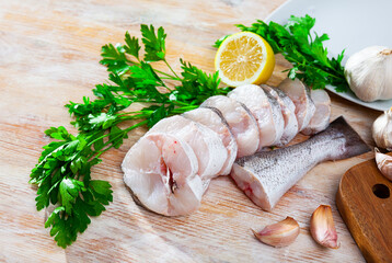 Wall Mural - Raw steaks of hake with lemon and greens ready for cooking on the wooden surface