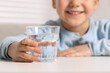 © New Africa - Little girl holding glass of fresh water at white table indoors, closeup