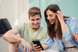 © Jose Calsina - Two teenage happy friends watching funny videos browsing on internet app with a smartphone and smiling together. Caucasian couple using a cell phone to post in a social media and chatting online. High