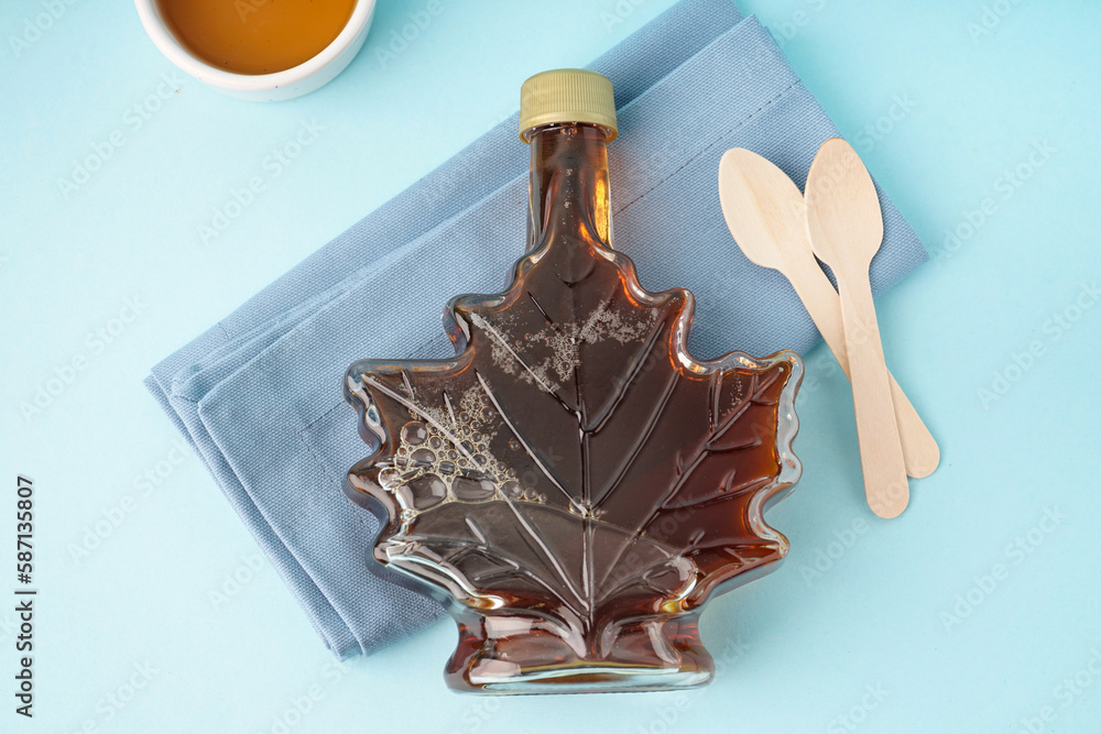 Bottle of tasty maple syrup on blue background