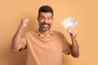 excited bearded man celebrating successful business money in beige background. finance, investment, offer, loan concept. 