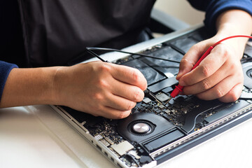 Computer technician wearing a mask A laptop motherboard repairman is using an IC meter to find defects on the motherboard for repair on his workbench. Board repair with modern technology