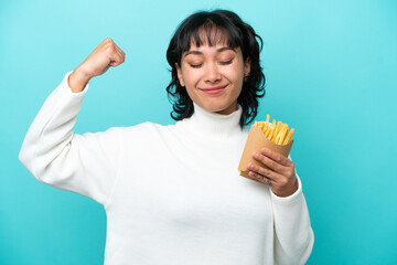 Sticker - Young Argentinian woman holding fried chips isolated on blue background doing strong gesture