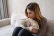 © Julija - young unhappy sadness girl sitting on sofa hugging pillow. She is feeling not very good due to her sickness and having a headache. Depression, mental health, Sad, tired.