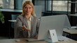 © Yuliia - Caucasian middle-aged woman HR manager recruiter leader female businesswoman at table working on computer making inviting gesture offer to sit interview invitation consultation motivation sitting down