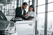 © standret - Man in formal clothes is consulting woman about the automobile in the car dealership