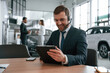 © standret - Man in headphones is sitting by table. Three people are working together in the car showroom
