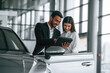 © standret - Showing information in the graphic tablet. Man in formal clothes is consulting woman about the automobile in the car dealership