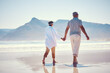 © Jesse Bettencourt/peopleimages.com - Holding hands, love and an old couple walking on the beach in summer with blue sky mockup from behind. Care, romance or mock up with a senior man and woman taking a walk on the sand by the ocean
