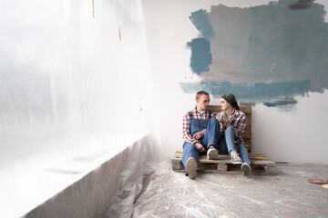 Young couple doing a repair in new home and relaxing with cup of coffee, copy space. Renovation, repair and relationship concept.