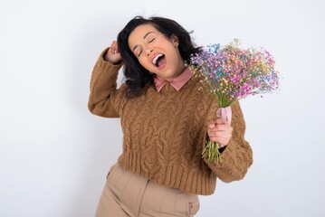 Photo of upbeat young woman holds big bouquet of nice flowers over white background has fun and dances carefree wear being in perfect mood makes movements. Spends free time on disco party