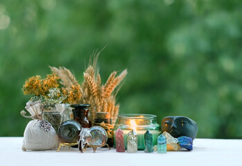 Poster - witchcraft items, candle, amulets, crystals close up on wooden table, blurred natural background. Wiccan magic practice. Witchcraft, esoteric spiritual ritual. Mysticism, divination, occultism theme.