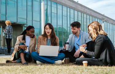 A group of four people sitting on the lawn chatting and discussing strategy outside an office building.