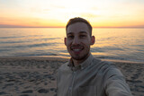 Fototapeta Paryż - young man in a shirt, taking a selfie in a sunset on the beach