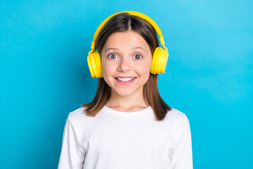 Photo of good mood schoolgirl with straight hairdo dressed white shirt headphones listen playlist isolated on blue color background