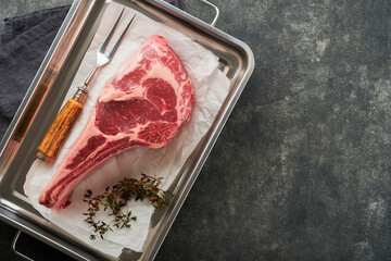 Wall Mural - Fresh tomahawk raw steak. Dry aged raw tomahawk beef steak with herbs and salt on old wooden background. Preparing to grill.  Top view and copy space.