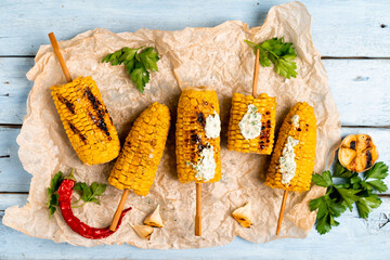 grilled corn on a blue wooden table with green sauce