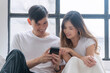© kaew6566 - Happy asian couple holding mobile phones search shopping online on app sitting together at home. Asian casual young lover using smartphone relax search something together in room. Lifestyle technology