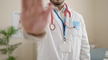 Wall Mural - Young hispanic man doctor doing stop sign with hand at clinic