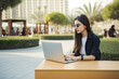 © MVProductions - Young woman with sunglasses sitting in Dubai and doing work on laptop. Student or freelancer lifestyle. High quality generative ai