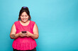 © Lux Images - Young curvy Latina woman in a pink sleeveless t-shirt, smiling and texting on her phone. Studio shot on blue background.