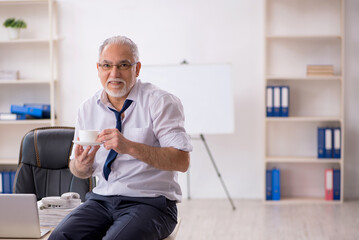 Wall Mural - Old male employee doing sport exercises at workplace