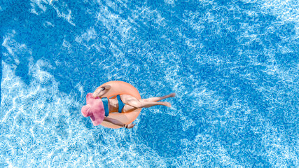 Wall Mural - Beautiful woman in hat in swimming pool aerial drone view from above, young girl in bikini relaxes and swims on inflatable ring donut and has fun in water on tropical vacation on holiday resort
