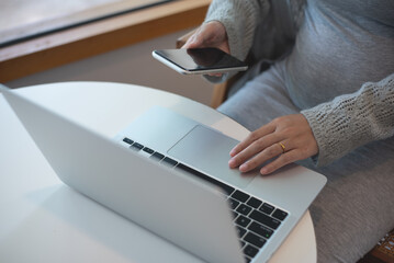 Canvas Print - Pregnant business woman sitting at table using mobile phone and working on laptop computer at cafe. pregnant woman online shopping via mobile app, close up