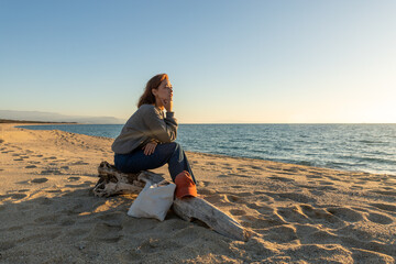 red-haired woman sitting on a log, watching the sunset on a beach