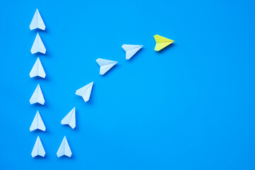 Wall Mural - Yellow paper airplane origami leading other white airplanes on blue background with customizable space for text or ideas. Leadership skills concept and copy space