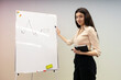 Handsome, smiling woman pointing to flipchart with marker, to graph. Successful businesswoman in modern office, indoors. Concept of business, education