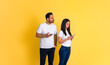 © Moon Safari - Possessive young adult man peeking at girlfriend's smart phone and trying to read her text messages while standing isolated on yellow background
