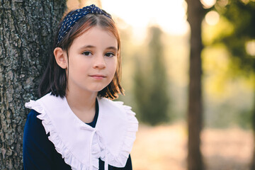 Wall Mural - Cute child girl 6-7 year old wear school dress with white collar outdoor over nature background. Looking at camera.