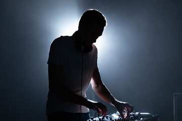 Wall Mural - Silhouette of a DJ performing on party in night club. Cool young man playing music on stage