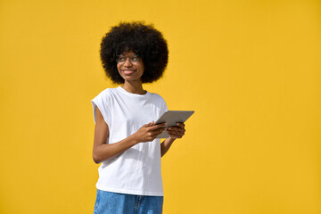 A happy hipster girl with afro haircut enjoy online communication and online services, scroll social media apps , look aside on tablet device isolated on yellow wall with place for copy space.