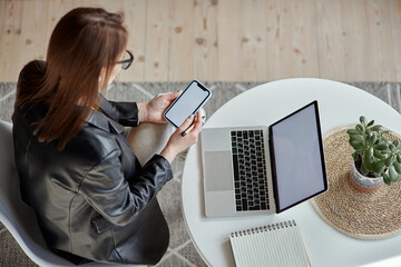 Wall Mural - Mockup white screen laptop and mobile phone woman using computer sitting at table at home, top view