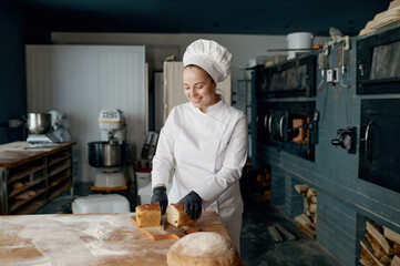 Baker chef holding knife and cutting fresh bread on wooden table