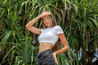 © kanashkin - An attractive woman in a white cropped t-shirt and shorts stands against the backdrop of palm trees.