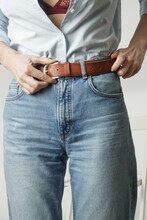 Fashion Portrait Of Young Woman In Cotton Button Down And Blue Jeans Ajusting Her Brown Leather Belt