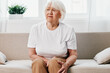 © SHOTPRIME STUDIO - Elderly woman severe pain in her leg sitting on the couch, health problems in old age, poor quality of life. Grandmother with gray hair holds on to her sore knee, problems with joints and ligaments.