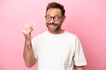 Wall Mural - Middle age man holding invisible braces isolated on pink background with happy expression