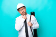 © luismolinero - Middle age architect man with helmet and holding blueprints isolated on blue background having doubts