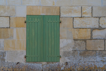 Green window shutters on a light block wall in France