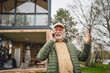 © Miljan Živković - One senior man stand in front of tiny house in day use smart phone